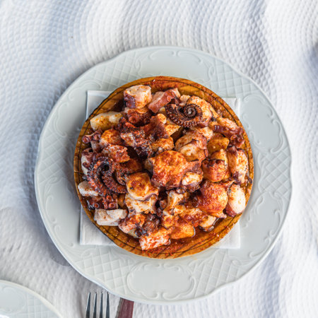 Galician-style octopus dish, served on its typical wooden plate; consists of cooked octopus slices, drizzled with olive oil, paprika and saltの写真素材