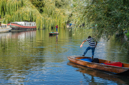 CAMBRIDGE, UK - OCTOBER 11, 2014: Punting on the River Cam in Cambridge, England. A punt is a flat-bottomed boat with a square-cut bow, designed for use in small rivers and shallow water. The punter propels the punt by pushing against the river bed with aのeditorial素材