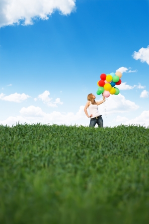 Happy young woman with colorful balloons on a green meadowの写真素材