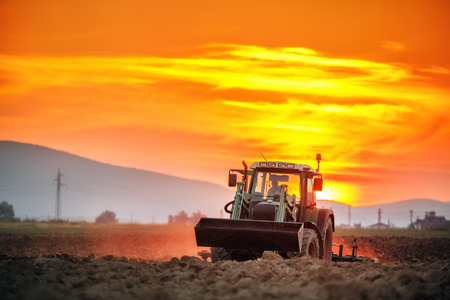 Tractor with cultivator handles field before planting, sunset shotの写真素材