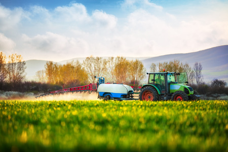 Farming tractor plowing and spraying on fieldの写真素材