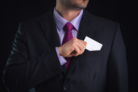 Businessman in elegant suit and with a tie, shows business card with copy space, studio shotの写真素材