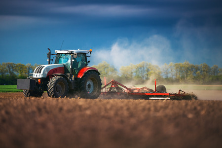 Farmer in tractor preparing land with seedbed cultivator, sunset shotの写真素材