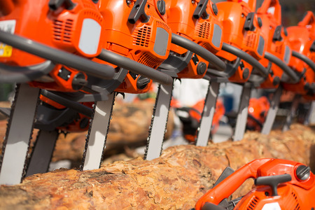 Electric chainsaw machines over heap of firewood outdoorsの写真素材