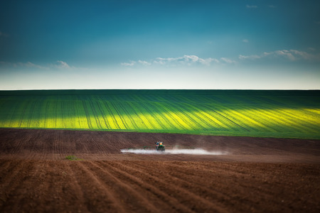 Farming tractor plowing and spraying on fieldの写真素材