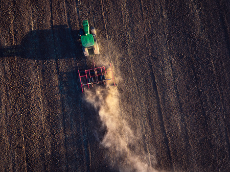 Farmer in tractor preparing land with cultivator, aerial view