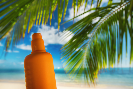 Bottle of sun protection lotion and palm leaf on the tropical beach