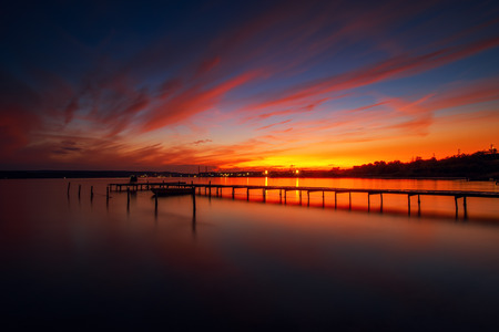 Wooden Dock and fishing boat at the lake, city lights at sunsetの写真素材