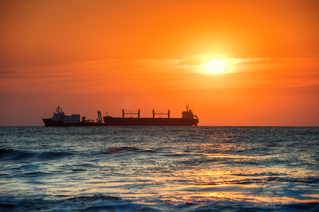 Sun setting at the sea with sailing cargo ship, scenic viewの写真素材