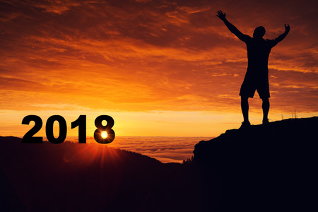 Man silhouette on the mountain top watching the sunrise and 2018 years while celebrating.の写真素材