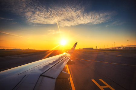 Airplane on the airport ready for flight and sunrise. Runway and plane wing.の写真素材