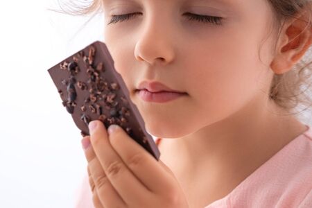 Beautiful little girl taste chocolate like a pro - breaking cacao bar, smelling, eating.の写真素材