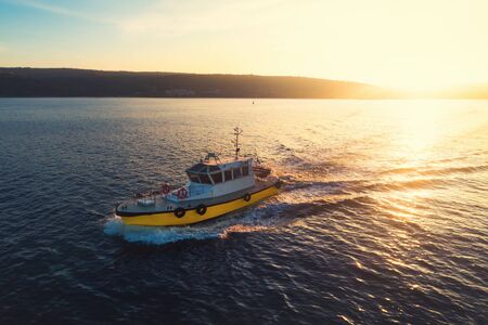 Patrol boat sailing at sunset in shining golden sea water.の写真素材