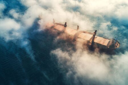 Cargo ship and cranes silhouettes in sea fog, crane vessel working for delivery of delivery...