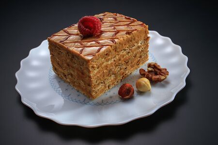Cake piece with nuts, chocolate, biscuits and caramel cream isolated on black background.