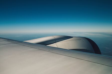 Wing of an airplane flying above the sky with clouds and city land.