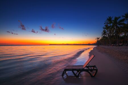 Deck chair on a empty tropical beach with palm trees at sunriseの写真素材