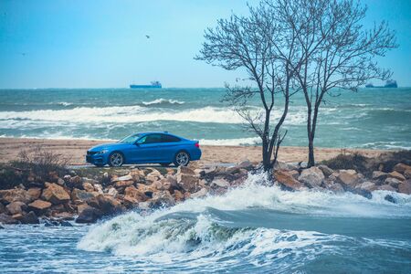 Waves crashing on the coast. Man driving sport car relaxing near beach. の写真素材
