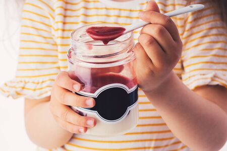Little girl eat milky dessert with cream and fruity jelly in a jar.の写真素材