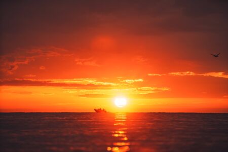 Silhouette of two people in a local small fishing boat moving with sunrise in the background.の写真素材