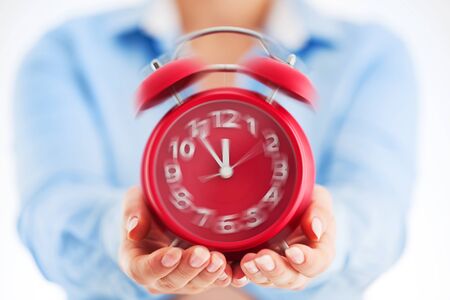 Business time concept. Woman holding red alarm clock in his hands close up.の写真素材