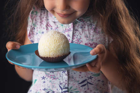 Beautiful little girl surprised from a tasty big chocolate coconut candy as a ball. Kid ready to eat...