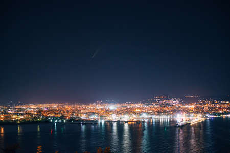Night view toward Varna, Bulgaria. Seascape with reflection of city lights and neowise in the starsの写真素材