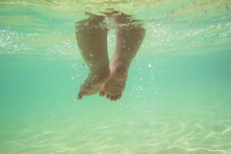 Little infant baby child legs and toes touch sand on sea beach, underwater viewの写真素材