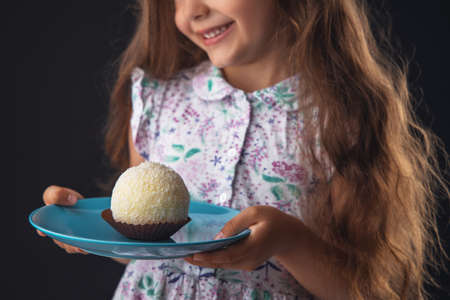 Beautiful little girl surprised from a tasty big chocolate coconut candy as a ball. Kid ready to eat cake.の写真素材