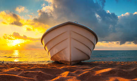 Tropical Seascape with a boat on sandy beach at cloudy sunrise or sunsetの写真素材