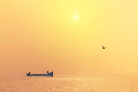 Fishing boat sailing in the sea during golden foggy morning. Beautiful ocean sunrise.の写真素材