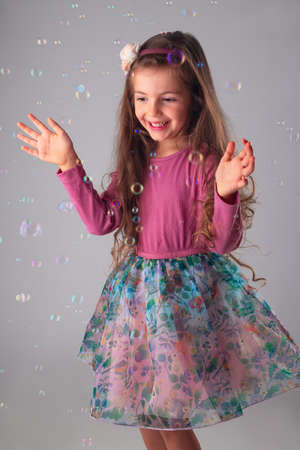 Happy little girl in party dress playing with soap bubbles portrait.の写真素材