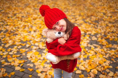 Happy little girl playing with his teddy bear toy in autumnal parkの写真素材