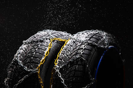 Winter Car tire with snow chains on black background. Winter season.の写真素材
