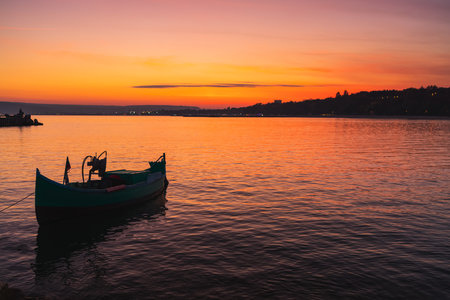 Fishing boat on shore and ripple sea water on dramatic colorful sunsetの写真素材