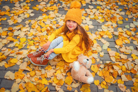 Happy little girl playing with his teddy bear toy in autumnal parkの写真素材