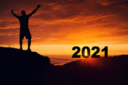 Man silhouette on the mountain top watching the sunrise and 2021 years while celebrating.の写真素材
