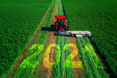 2021 Happy Ney Wear concept and red tractor mowing green field.の写真素材