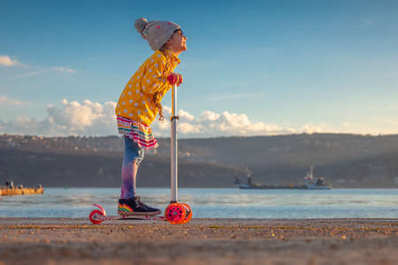 Little girl riding scooter outdoor near sea harbourの写真素材