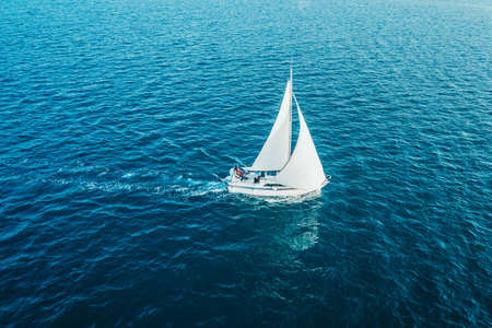 Sailing ship yacht with white sails at opened sea. Aerial - drone view to sailboat in windy condition.の写真素材