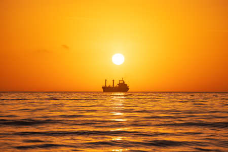 Sun setting at the sea with sailing cargo ship, scenic viewの写真素材