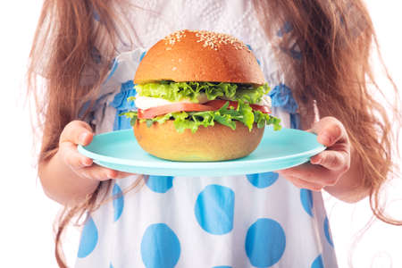 Little girl eating big burger. Kid looking at healthy big sandwich, studio isolated on white background.の写真素材