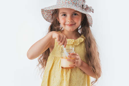 Beautiful little girl eating tasty cream dessert portrait isolated on white background.の写真素材