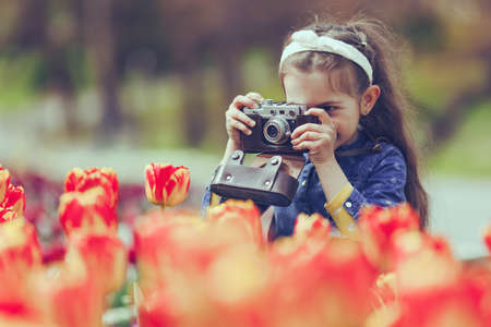Little girl with old vintage camera making photos of tulips in flowers garden.Vintage colorの写真素材