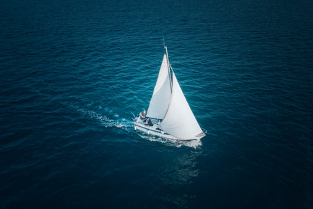 Sailing ship yacht with white sails at opened sea. Aerial - drone view to sailboat in windy condition.の写真素材