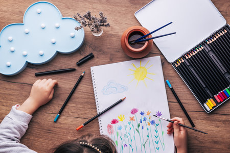 Child drawing top view. Artwork workplace with creative accessories. Drawing sheet with artwork by daughter on tableの写真素材
