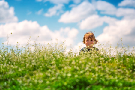 Happy baby boy enjoying spring green grass with daisy flowers in a fieldの写真素材