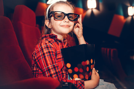 Little girl watching cartoon 3D movie in cinema and eating popcornの写真素材