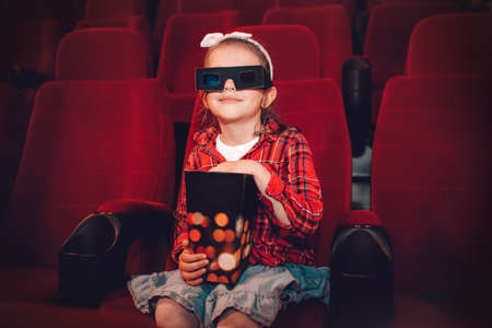 Little girl watching cartoon 3D movie in cinema and eating popcornの写真素材
