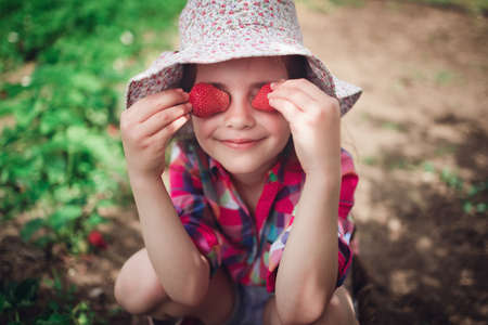 Little girl picking strawberry on a farm field.  Strawberry in a kid hand against background of flowers.の写真素材